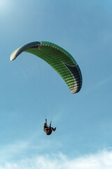 Bottom view of green paraglider flying among blue sky on a sunny day.