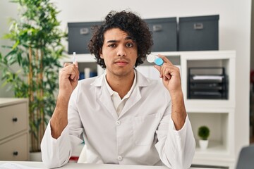 Hispanic man with curly hair holding contact lenses skeptic and nervous, frowning upset because of...