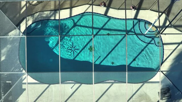 Typical contemporary american big swimming pool on backyard of private house with outside lanai enclosure covering. Concept of outdoor living and having fun in warm pool water on Florida summer sun