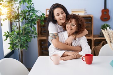 Two women mother and daughter drinking coffee hugging each other at home