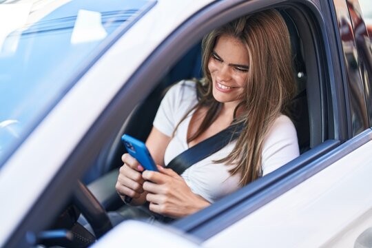 Young woman using smartphone sitting on car at street