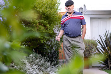 Retired old man enjoy watering his outdoor plants and whistles