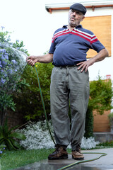 Senior gray hair man enjoys watering and whistling at his home backyard