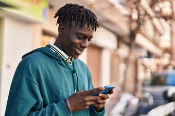 Fototapeta na wymiar African american man smiling confident using smartphone at street