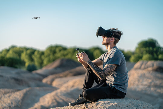 Tattooed Caucasian man flying drone with modern Virtual Reality fpv headset in arid desert area