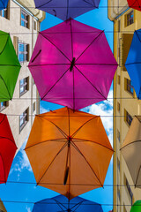 Ulica Piotrkowska w Łodzi i kolorowe parasole wiszące między budynkami nad błękitnym niebem. - obrazy, fototapety, plakaty