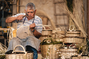 Senior Latin American man using hammer while doing wicker baskets at his workshop