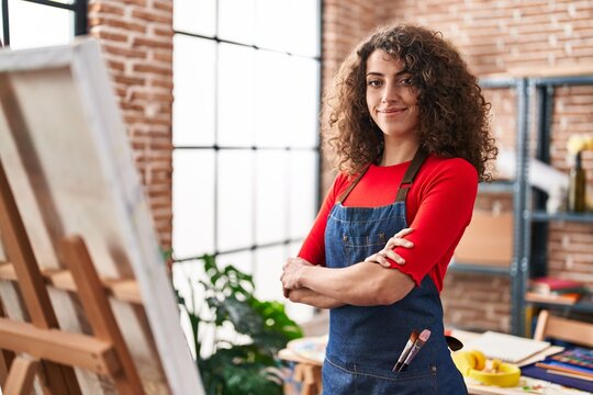 Young hispanic woman artist smiling confident standing with arms crossed gesture at art studio