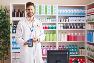 Young caucasian man pharmacist smiling confident using credit card and data phone at pharmacy