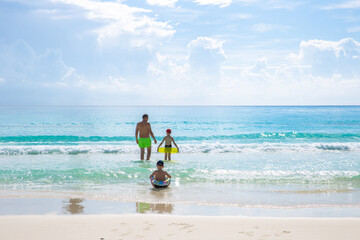 Oudoor summer activity. Concept of fun, health and vacation. A happy family: father and two sons with inflatable rings swimming in the ocean on a hot summer day. Cancun, Mexico.