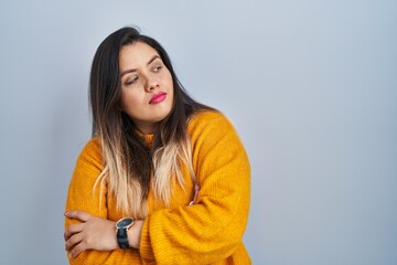 Young hispanic woman standing over isolated background looking to the side with arms crossed convinced and confident