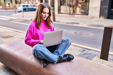 Young woman using laptop sitting on bench at street