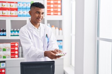Naklejka na ściany i meble Young latin man pharmacist smiling confident holding pills at pharmacy