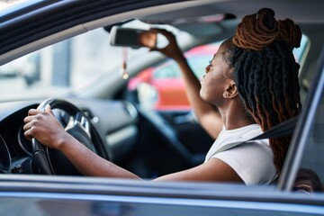 Fototapeta na wymiar African american woman touching rearview sitting on car at street