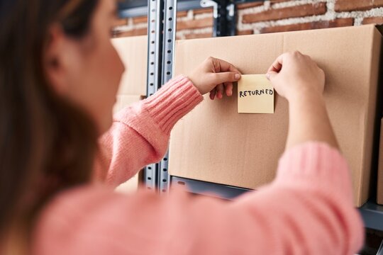 Young beautiful hispanic woman ecommerce business worker putting returned reminder paper on package at office