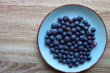 Turquoise plate with fresh blueberries on wooden background. Top view.