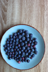 Turquoise plate with fresh blueberries on wooden background. Top view.