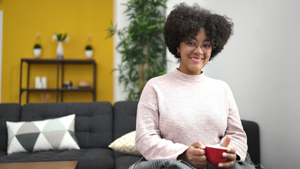 Young african american woman drinking tea sitting on sofa at home