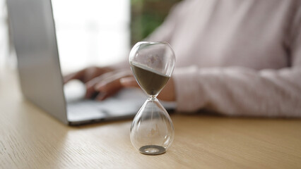 Young african american woman business worker using laptop controlling time with hourglass at office