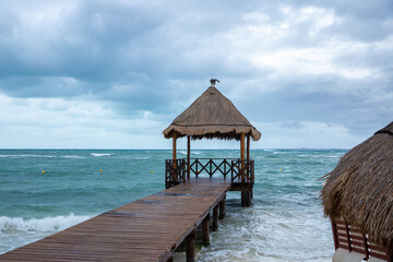 Tropical gazebo with a bridge over the ocean with a pelican sitting on it. Tropical storm in the Atlantic Ocean. Beautiful hotel zone, resort, bed wheather. Hurricane in Caribbean Sea, Mexico, Cancun.