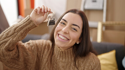 Naklejka premium Young beautiful hispanic woman holding keys sitting on sofa at new home