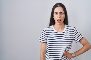 Young brunette woman wearing striped t shirt in shock face, looking skeptical and sarcastic, surprised with open mouth