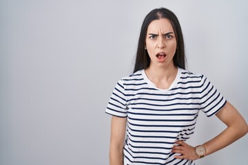 Obraz premium Young brunette woman wearing striped t shirt in shock face, looking skeptical and sarcastic, surprised with open mouth