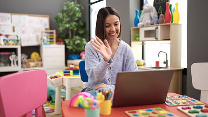 Young beautiful hispanic woman working as a teacher having video call at kindergarten