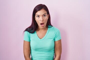 Young hispanic woman standing over pink background afraid and shocked with surprise and amazed expression, fear and excited face.