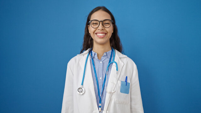 Young beautiful hispanic woman doctor smiling confident standing over isolated blue background