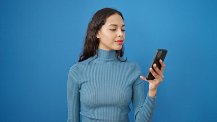 Young beautiful hispanic woman using smartphone over isolated blue background