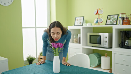 Fototapeta na wymiar Young beautiful hispanic woman smelling flowers in a vase at home