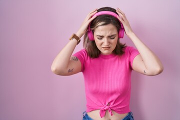 Blonde caucasian woman listening to music using headphones suffering from headache desperate and stressed because pain and migraine. hands on head.