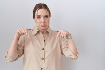 Young caucasian woman wearing casual shirt pointing down looking sad and upset, indicating...