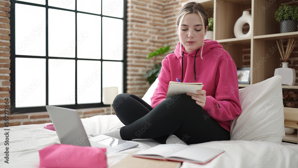 Sticker young blonde woman student writing on notebook studying on bed at bedroom