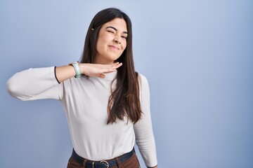 Young brunette woman standing over blue background cutting throat with hand as knife, threaten aggression with furious violence