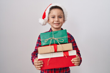 Little hispanic boy wearing christmas hat holding presents smiling with a happy and cool smile on...