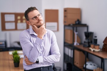 Young hispanic man at the office with hand on chin thinking about question, pensive expression....