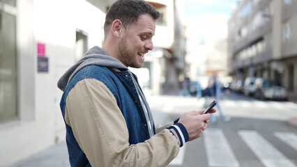 Young caucasian man smiling using smartphone at street