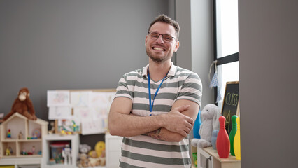 Young caucasian man working as teacher smiling with crossed arms at kindergarten