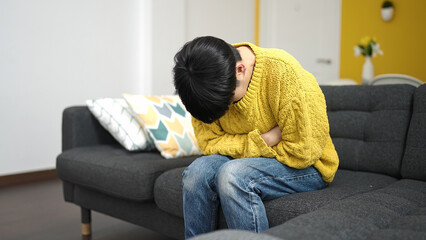 Young chinese woman suffering for stomach ache sitting on sofa at home