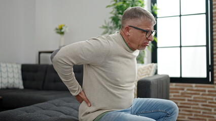 Fototapeta premium Middle age grey-haired man suffering for backache sitting on sofa at home