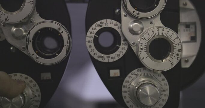 close up on finger doing micro adjustment on lens then turning knob making optics change of phoroptero ophthalmic machine, dark room