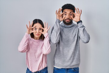 Young hispanic couple standing together trying to open eyes with fingers, sleepy and tired for morning fatigue