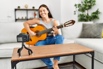 Young beautiful hispanic woman having playing classical guitar recording video at home