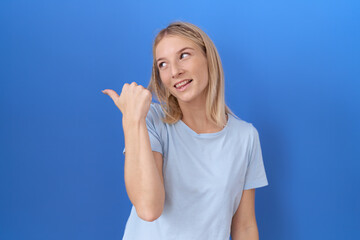 Fototapeta premium Young caucasian woman wearing casual blue t shirt smiling with happy face looking and pointing to the side with thumb up.