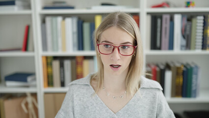 Young blonde woman sitting with surprised expression at library university