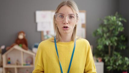 Young blonde woman preschool teacher with angry face at kindergarten