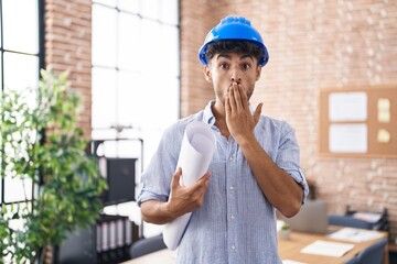 Arab man with beard wearing architect hardhat at construction office covering mouth with hand,...