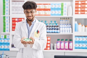 Young arab man pharmacist smiling confident holding capsules at pharmacy